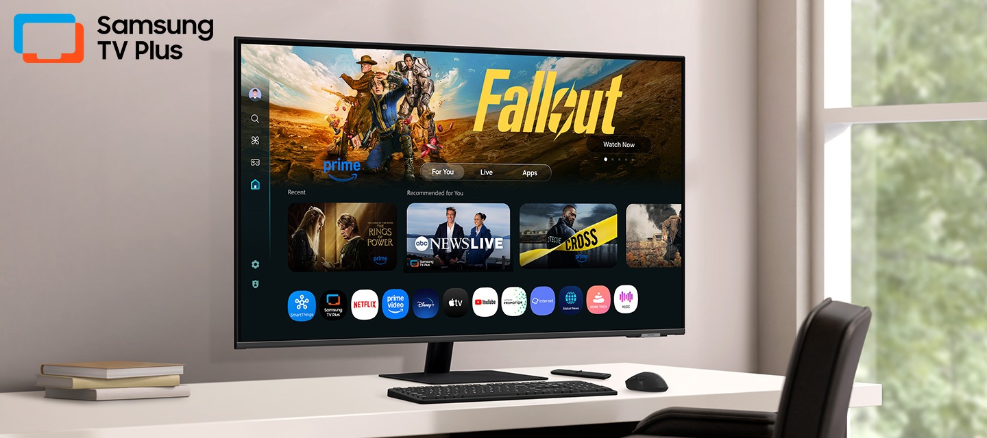 Monitor on desk displays Smart TV Apps page with various content and apps lined up. Samsung TV Plus logo.