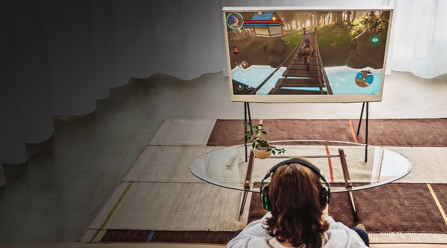 A man is sitting and playing a game on his console while watching the TV screen.