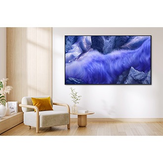 A QLED TV is installed on the wall of a living room. The screen shows an abstract grassy landscape in vivid blue and purple tones.
