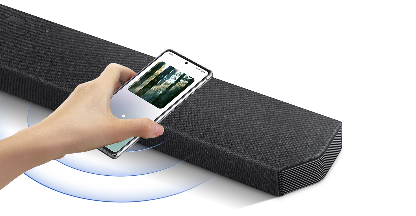 A hand taps a smartphone with the Samsung music app on-screen on the soundbar and the soundbar instantly plays music, showing how easy it is to switch from smartphone to soundbar.