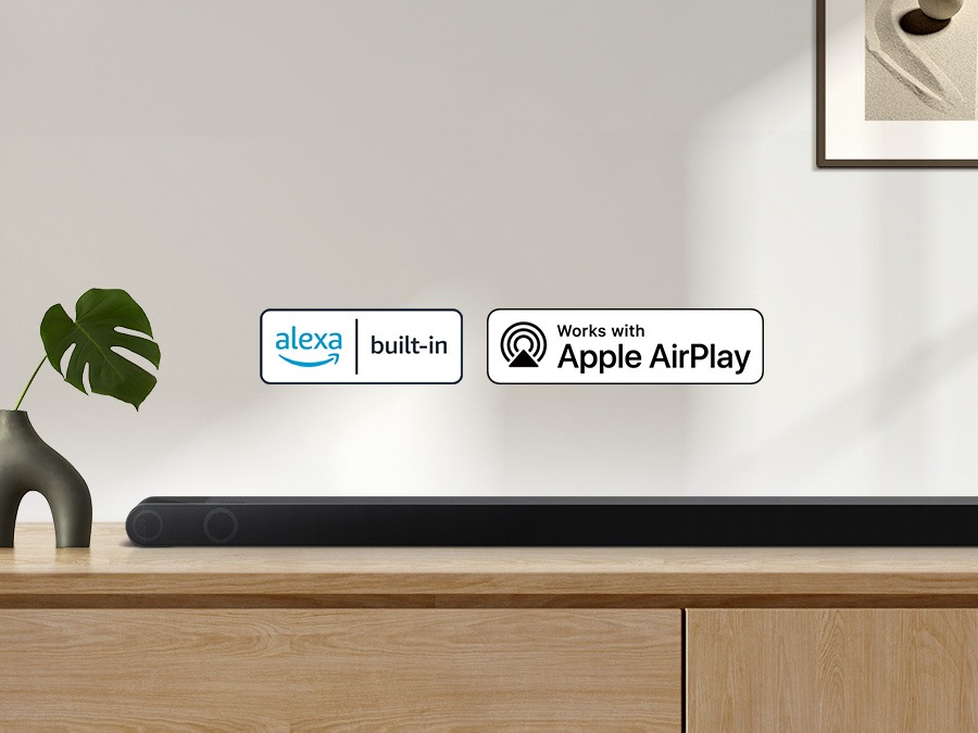 Logotip Alexa in logotip Apple AirPlay je mogoče videti skupaj z zvočno vrstico Samsung S800B, ki sedi na omari v dnevni sobi.