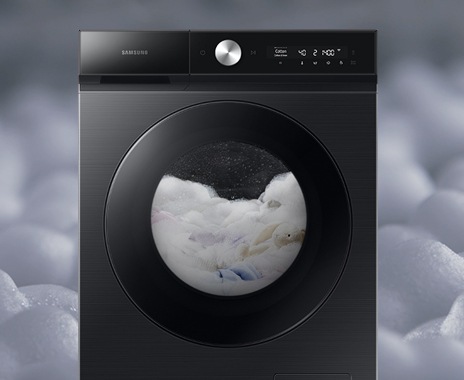A front facing white Samsung Bespoke Grande AI washer is set with detergent foam. The washer is in mid-cycle, with laundry and detergent bubbles inside the machine.