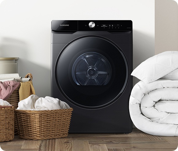 A white Bespoke Grande AI dryer is in a laundry room. Three baskets of laundry are placed to the left of the machine, and folded white bedding is placed to the right of the machine.