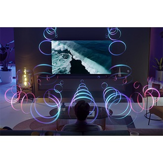 ชายคนหนึ่งกำลังดูทีวี Samsung พร้อมด้วยซาวด์บาร์ Samsung ระบบ Q-Symphony จะซิงค์เสียงจากทีวีและซาวด์บาร์เพื่อเล่นเสียงอย่างสอดประสานกัน