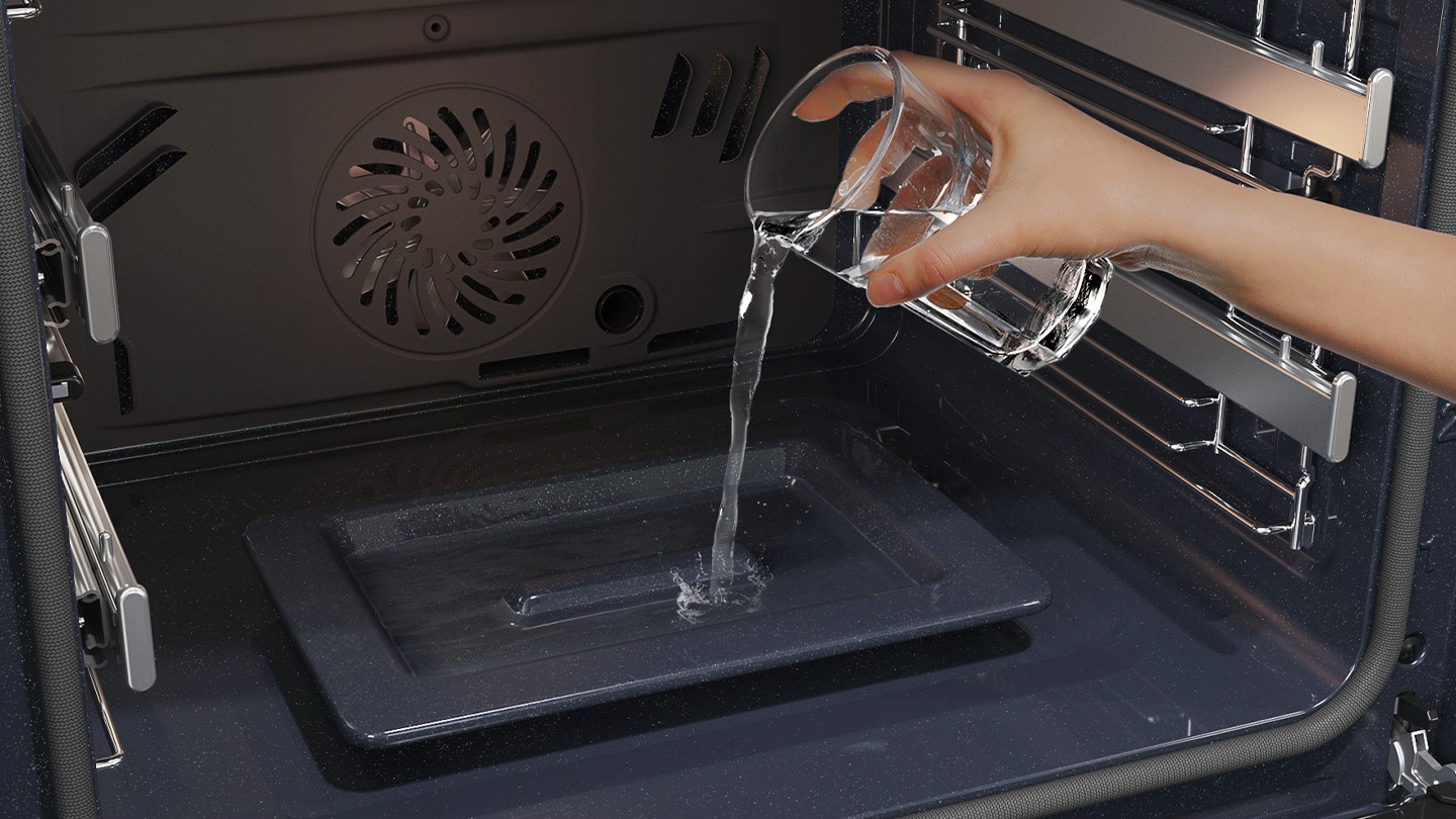 Shows a person pouring water from a glass into a dedicated tray on the bottom of the oven, which is used to create steam.