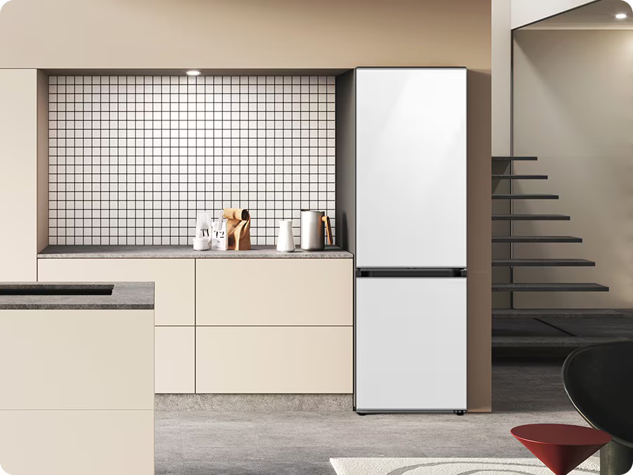 A Bespoke refrigerator with a Glam White glass top and a Satin beige glass bottom is built into a beige cabinet in a minimally decorated kitchen.