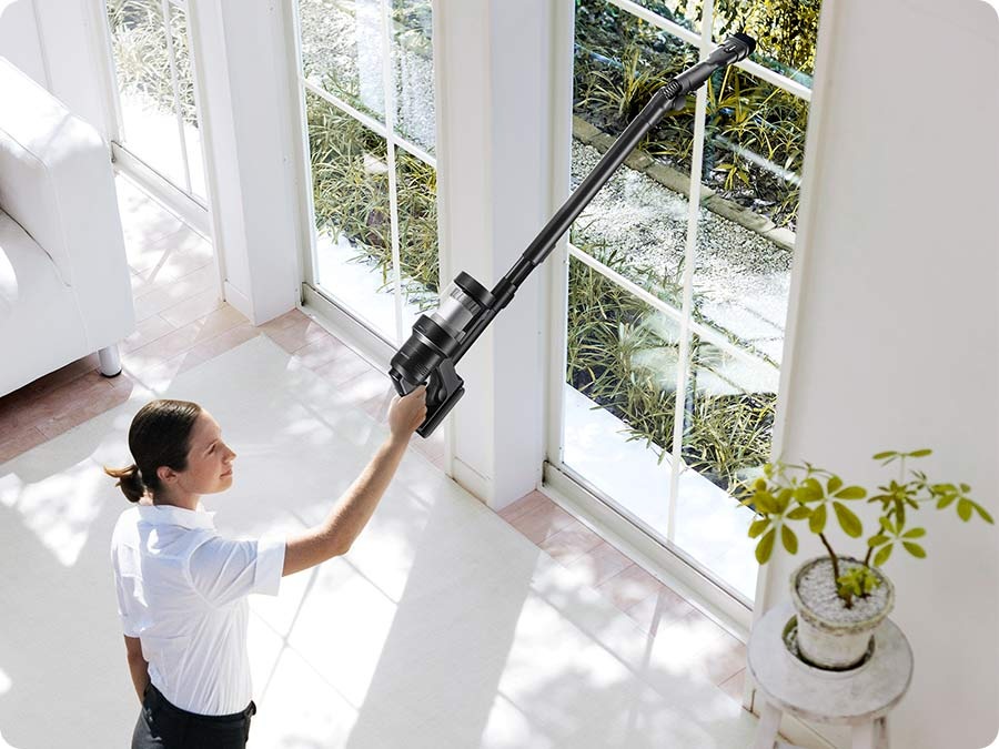 A woman vacuums a high window sill with a Bespoke Jet™ AI.