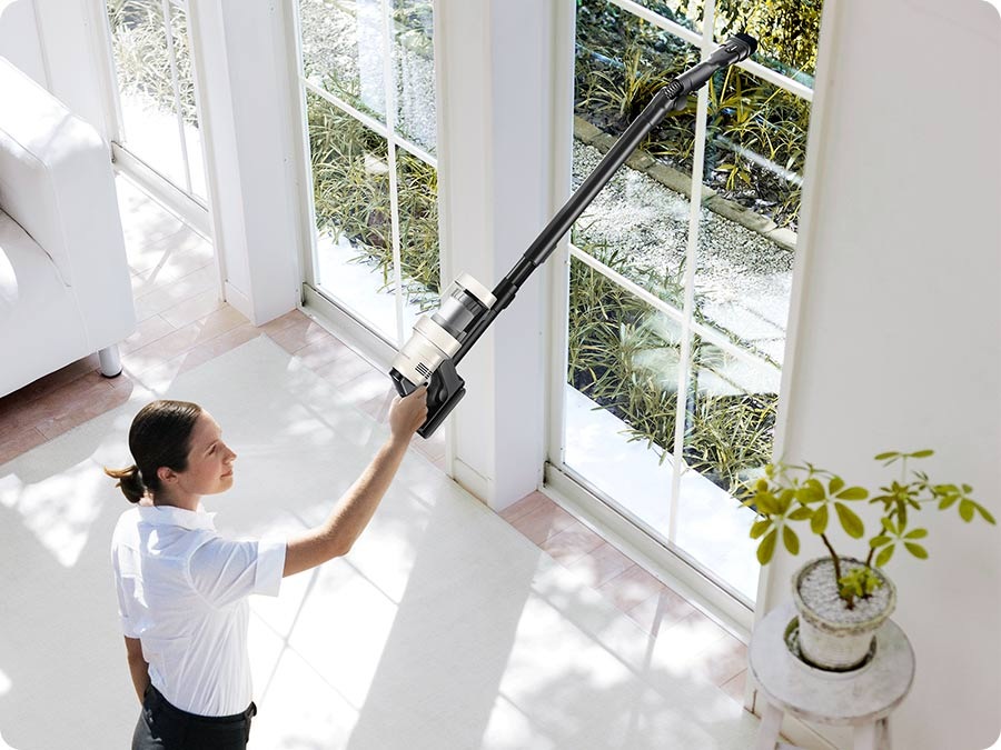 A woman vacuums a high window sill with a Bespoke Jet™ AI.