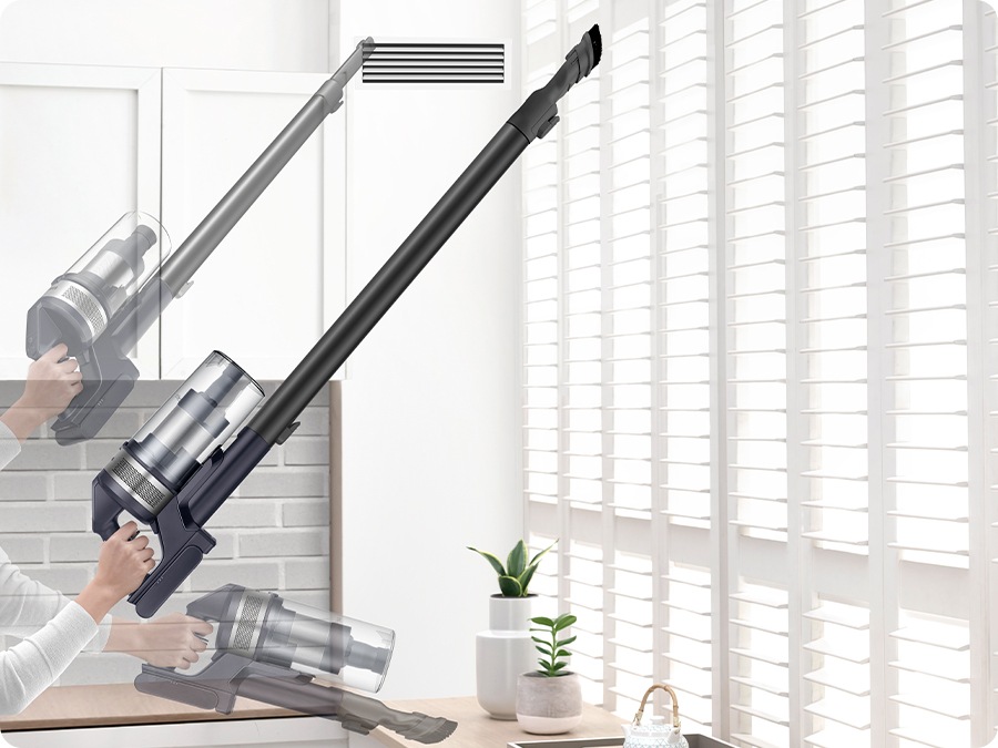 A person lifts Jet 75E with one hand and cleans vent with the crevice tool and cleans blinds and table with the combination tool.