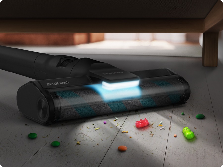 There is a Jet 85 with a slim LED Brush reaches underneath a sofa to vacuum dirt. LED lighting is on.
