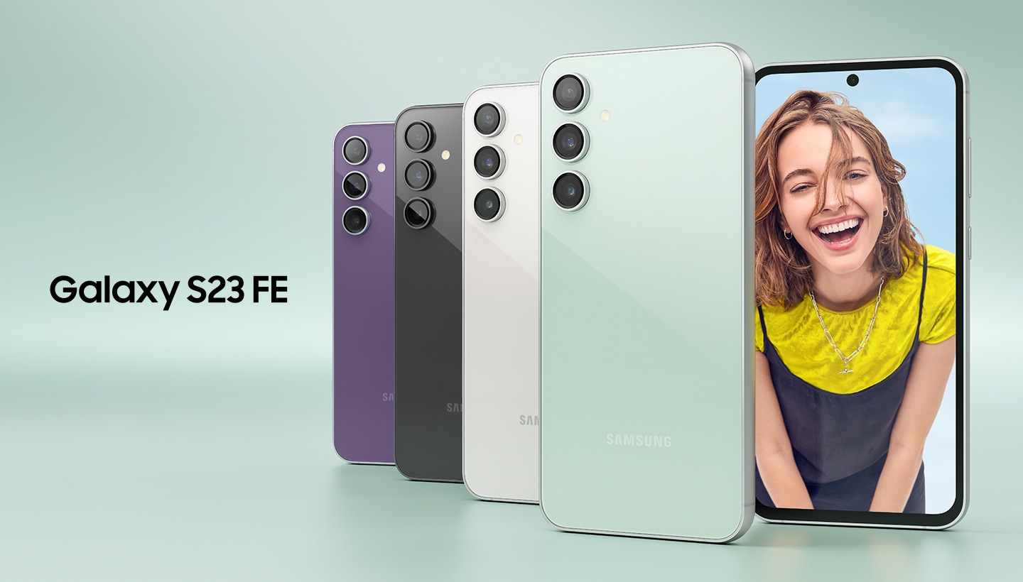 Five Galaxy S23 FE devices in Purple, Graphite, Cream and Mint. Four are seen standing upright from the rear overlapping on top of each other. The other one is seen from the front with a woman up-close onscreen smiling at the camera.