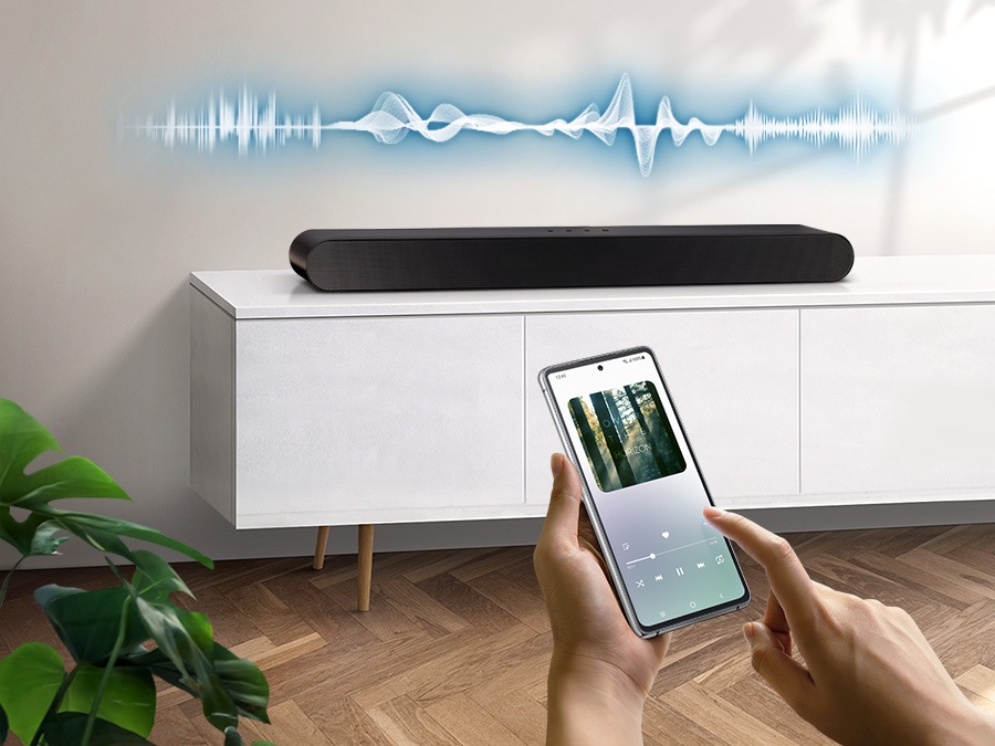 User plays music on their smartphone directly from their soundbar, which has soundwave graphics above it, using Music Mode which allows easy smartphone connectivity so optimized sound can be heard from soundbar.