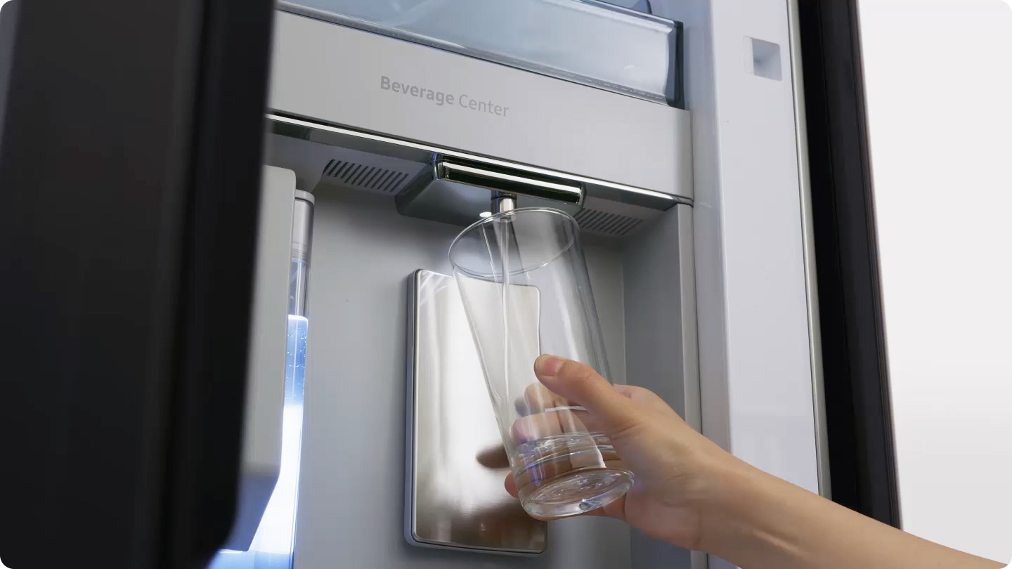 A close-up of a water pitcher with sliced limes being filled by the Bespoke refrigerator's water dispenser transitions to a hand holding a glass being filled by the dispenser. The nozzle of the dispenser can be easily removed for cleaning.