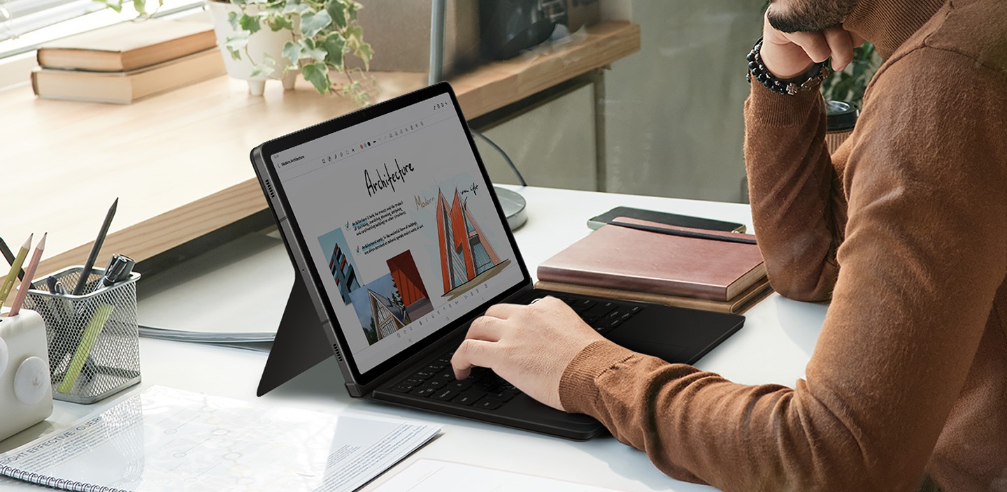 Galaxy Tab S9 kullanan bir adamın eli Book Cover Keyboard’un klavyesi üzerinde görülüyor.