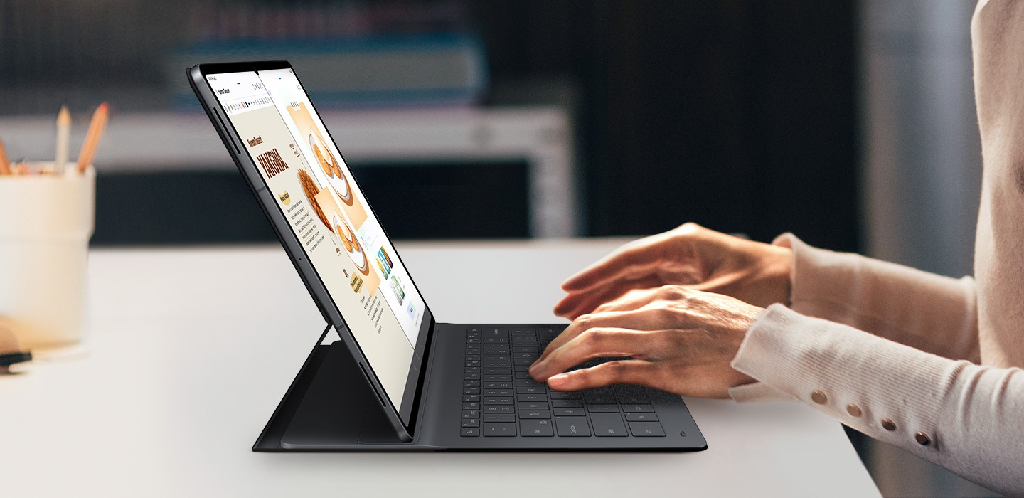A person types on Galaxy Tab S11 Ultra using Book Cover Keyboard Slim. The screen displays Drawing Assist and Samsung Notes open side by side. The keyboard's sleek fit complements the tablet's design, highlighting a clean, professional setup for creative multitasking.