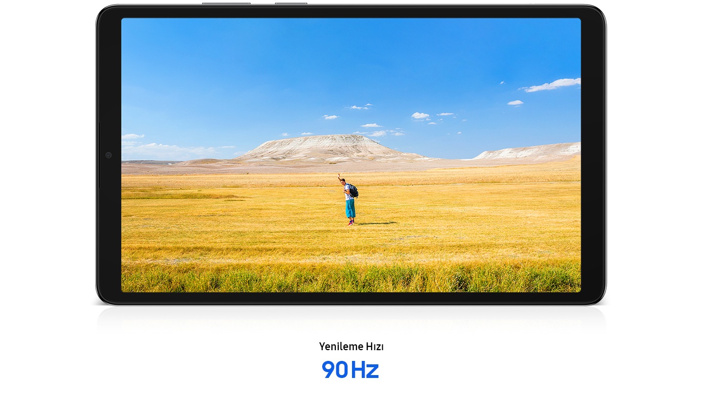 Yatay olarak yerleştirilmiş Galaxy Tab A11’in ekranında, ellerini sallayan bir adamın özgür ruh halini çağrıştıran net görüntüsü gösteriliyor. Arka planda mavi bir gökyüzü, sarı ve kahverengi çimlerden oluşan geniş bir ufukta uzanıyor. Tabletin altında “Yenileme Hızı 90 Hz” metni görülüyor.