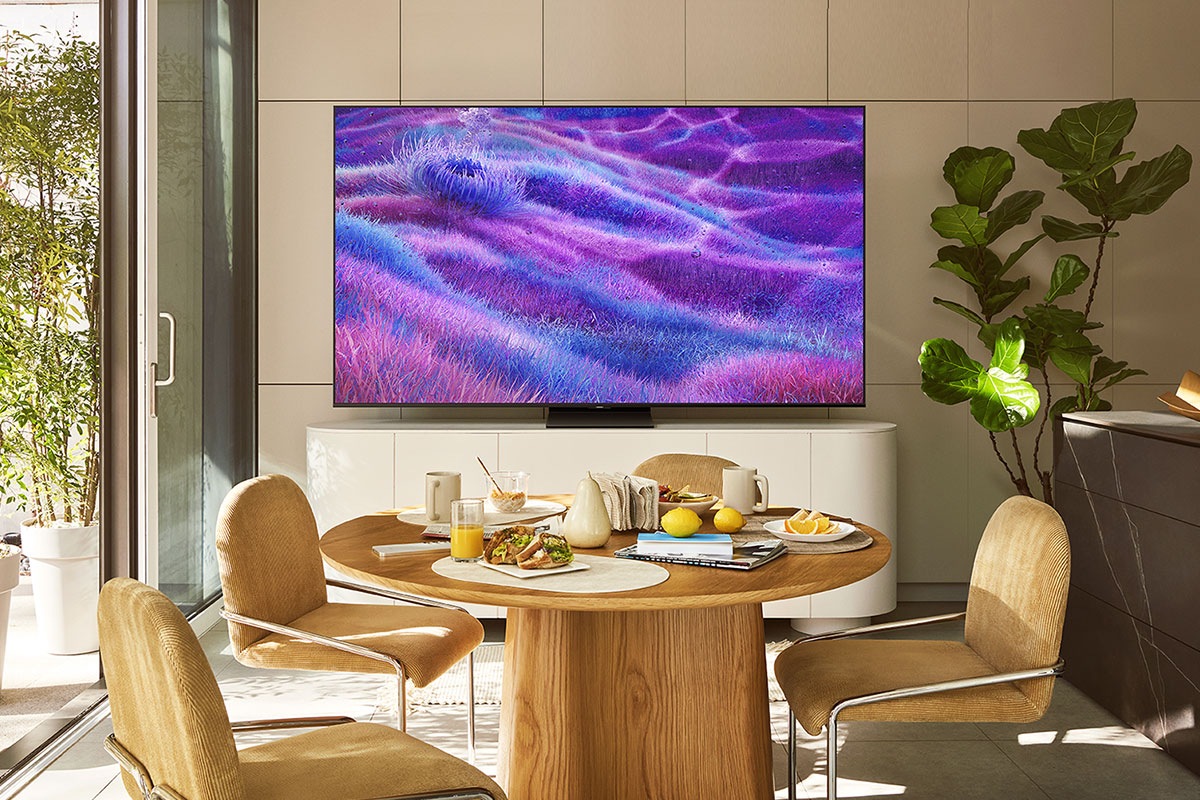 Güneşli bir mutfakta televizyon, mavi ve morun canlı tonlarında çimenli bir manzaradan gerçek dışı bir sahne gösteriyor.