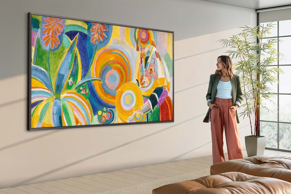 Aydınlık ve modern bir oturma odasında sanat eseri sergileyen 98 inçlik büyük The Frame TV ve yanında durup eseri inceleyen bir kişi.