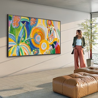Aydınlık ve modern bir oturma odasında sanat eseri sergileyen 98 inçlik büyük The Frame TV ve yanında durup eseri inceleyen bir kişi.