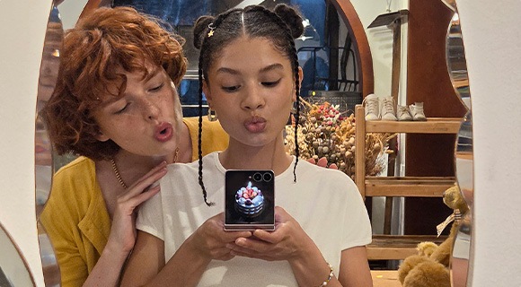 Aynada selfie çeken iki kişinin portresi. Kapak ekranında kişiselleştirilmiş bir fotoğrafla Galaxy Z Flip8’i FlexMode’da tutan bir kişi görülüyor.