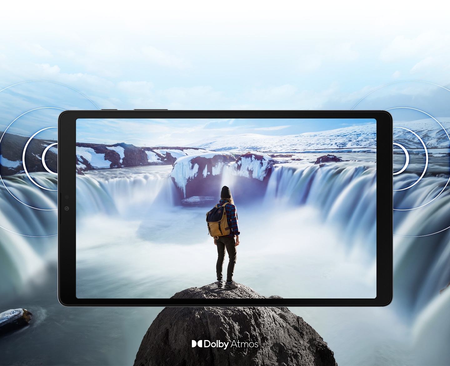 從正面觀看橫放的 Galaxy Tab A7 Lite，螢幕顯示一個人站在奔騰瀑布前的岩石上。圖像超出平板邊框，展示更大的顯示範圍。平板兩側如漣漪般波紋，展示雙喇叭的位置及 Dolby Atmos 環繞音效。