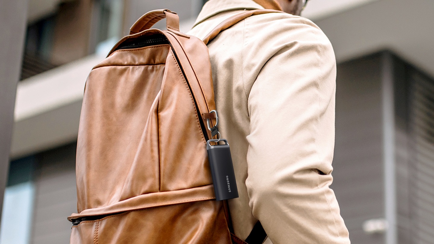 照片顯示一名男子背著米色背包，背包右方吊掛著一台移動固態硬碟 T5 EVO USB 3.2 Gen 1。