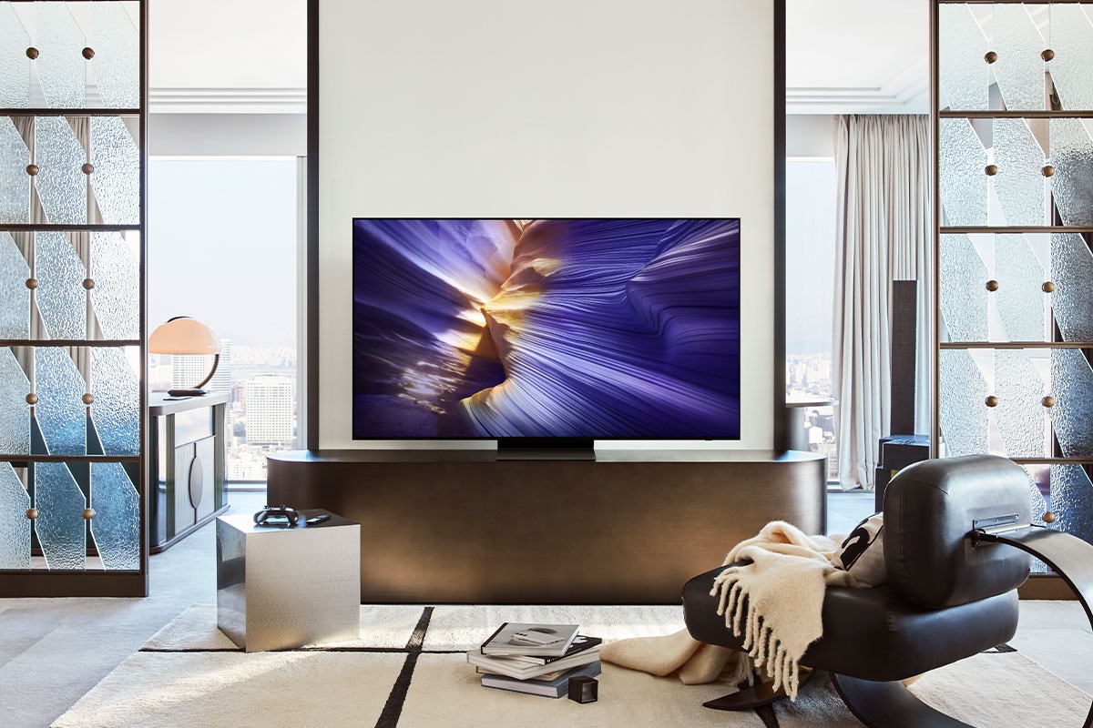 一台 Samsung OLED 智慧顯示器擺放在客廳的電視櫃上，螢幕上呈現出一幅抽象的紫色風景畫面。