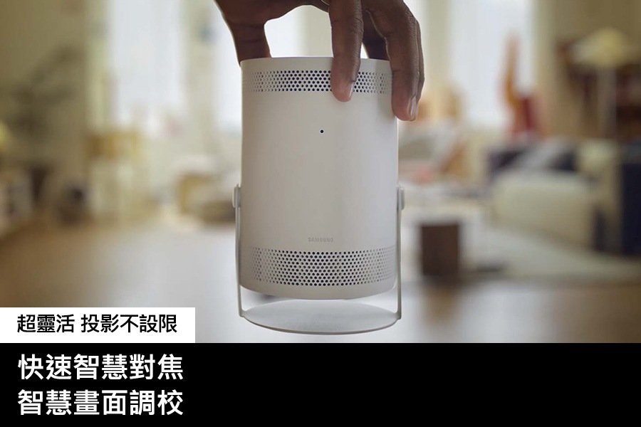 [一個人拿著 Thé F~réés~týlé~ 微型智慧投影機，將其放置在螢幕的前面和中間。畫面中客廳的背景是模糊的。]