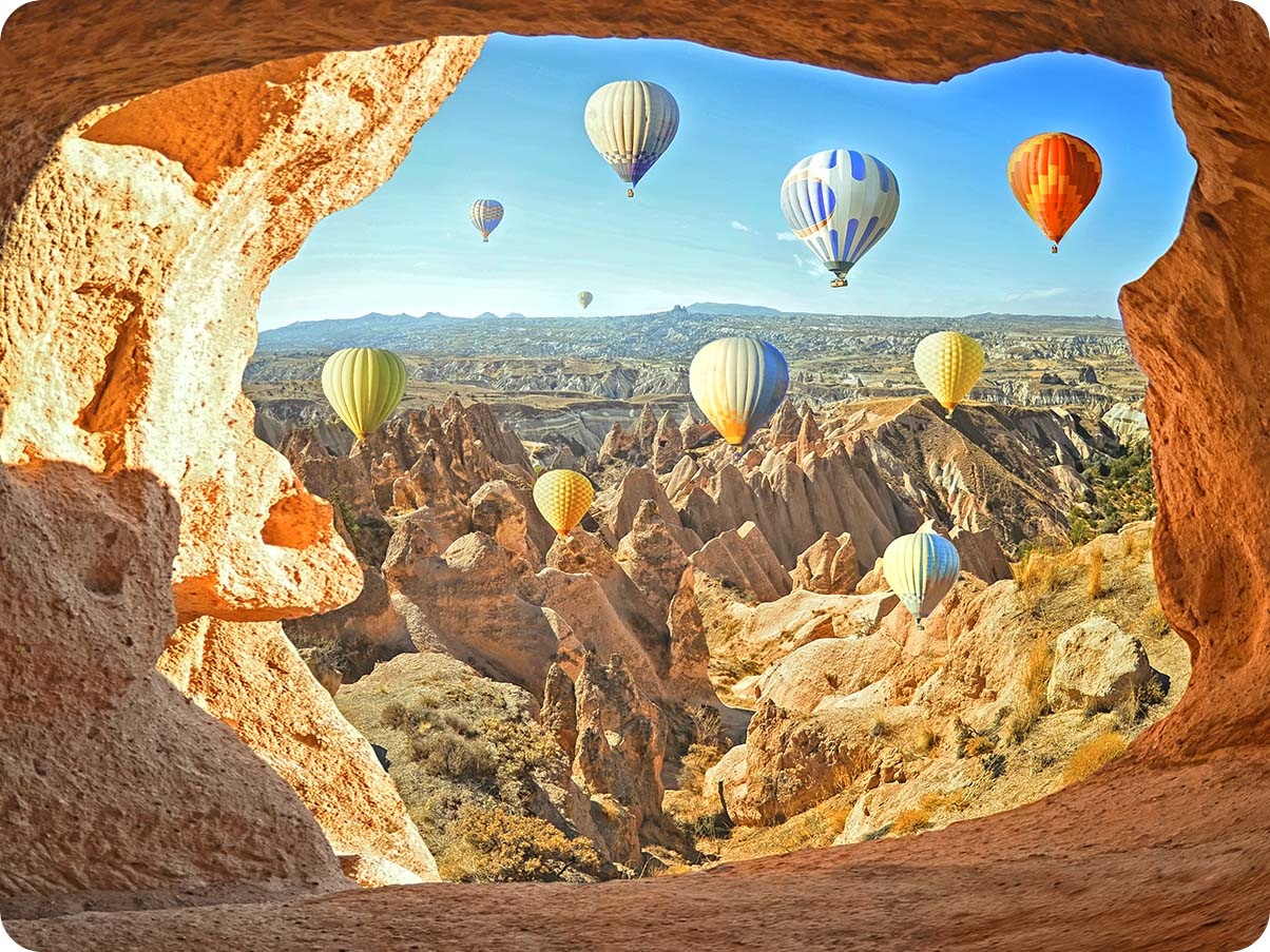 Photo taken with Ultra Wide Camera shows colorful air balloons in the sky and a vast landscape in the background. With the Ultra-wide angle icon above activated, the edges of the shot include the cave where the shot was taken.