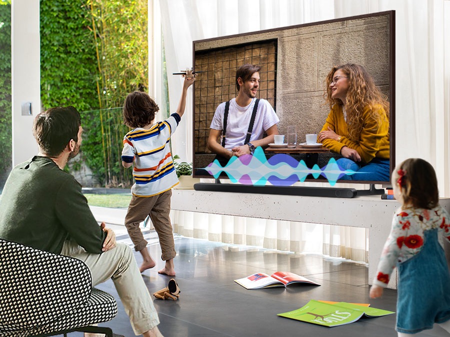 A man watches TV while his children play. Simulated sound wave graphics show Active Voice Amplifier technology optimizing dialogue so it can be heard more clearly in noisy environments.