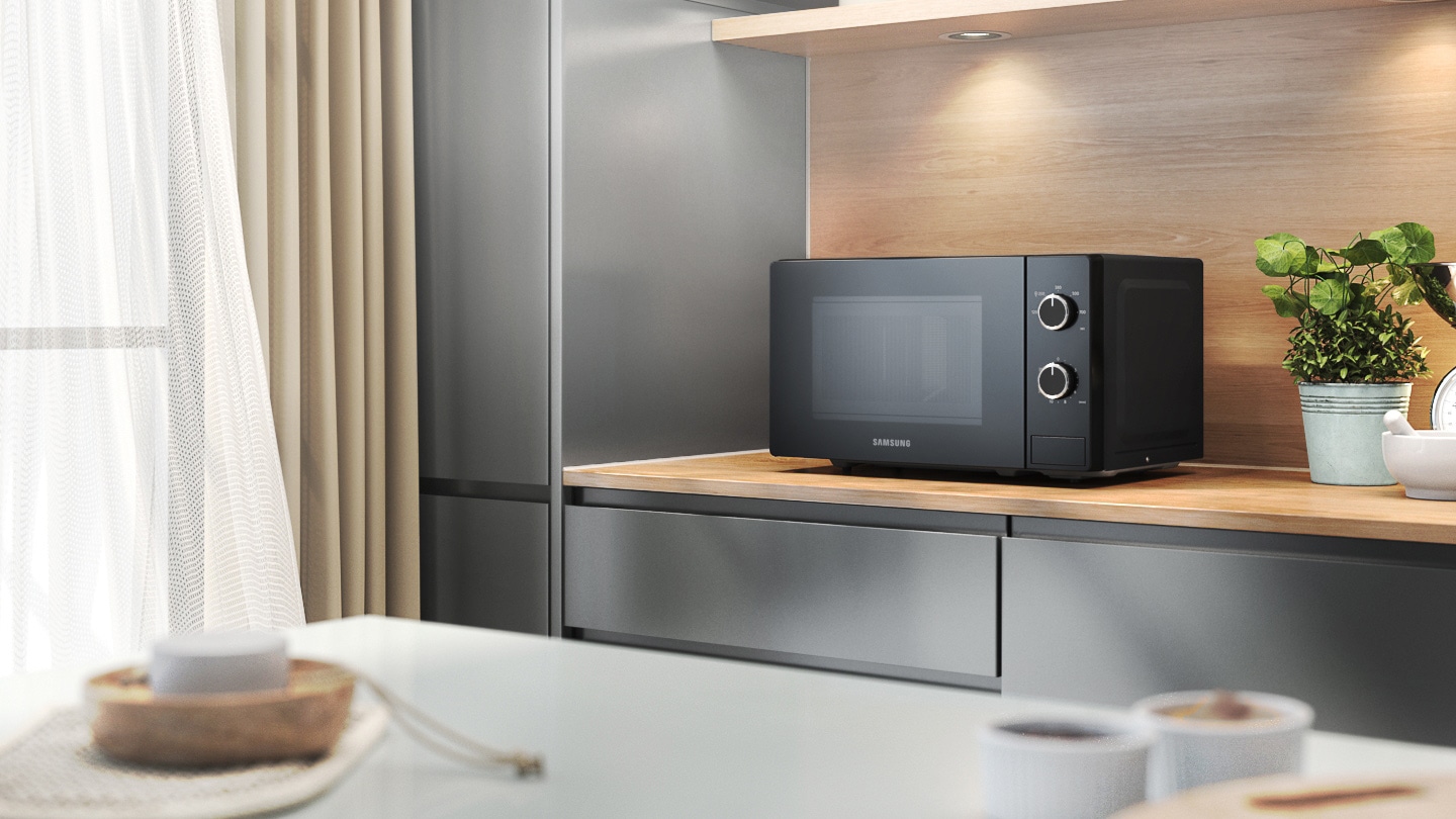 Shows the microwave oven on a kitchen worktop, surrounded by various household items and kitchenware.