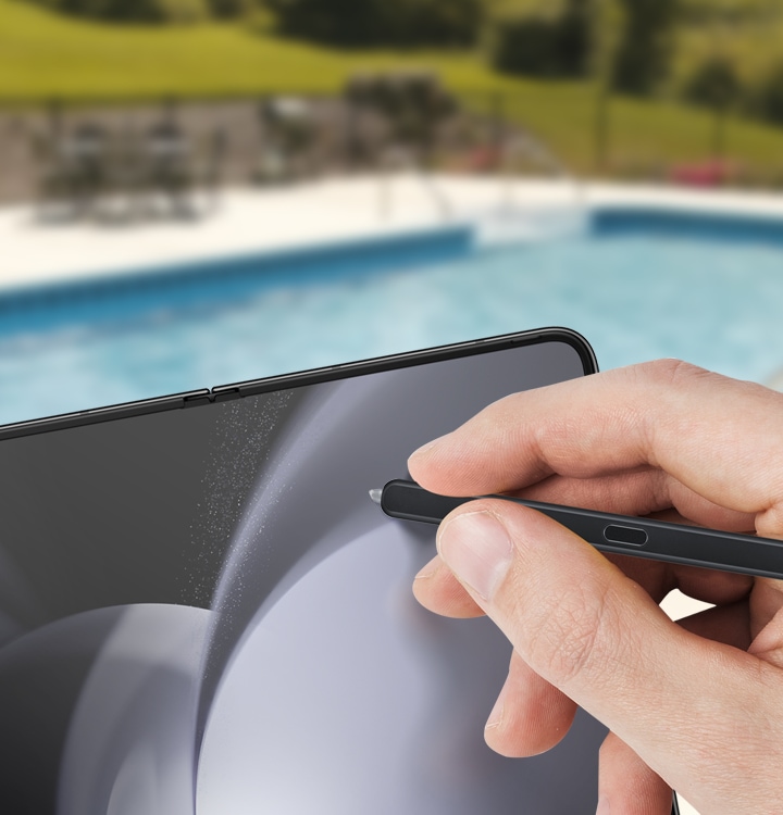 A hand is shown using a Galaxy Z Fold5 S Pen Fold Edition on a device near a swimming pool to highlight the pen's water resistant feature.
