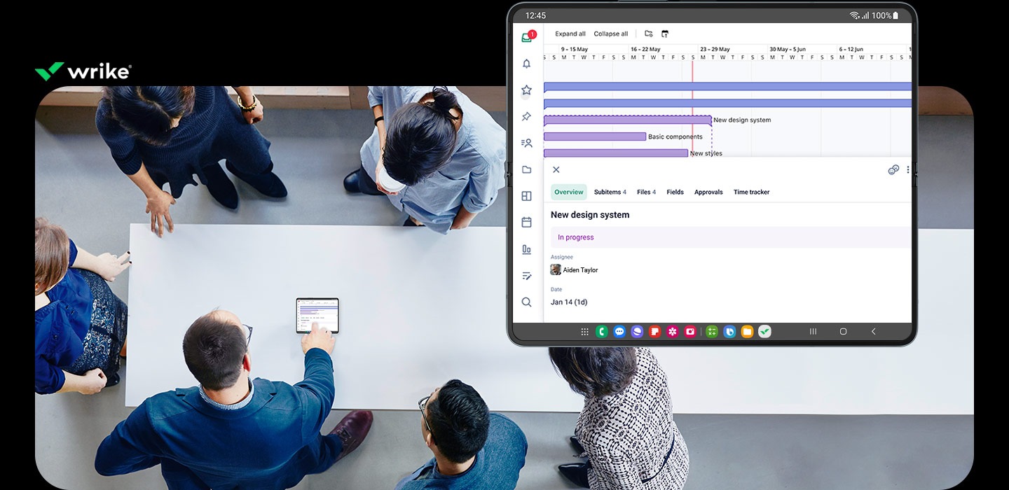 La aplicación Wrike está abierta en la pantalla principal del Galaxy Z Fold5. Muestra un gráfico de flujo de trabajo del proyecto. Un grupo de empleados se reúne alrededor de un Galaxy Z Fold5 abierto sobre una mesa y observa un gráfico en la pantalla. Logotipo de Wrike.