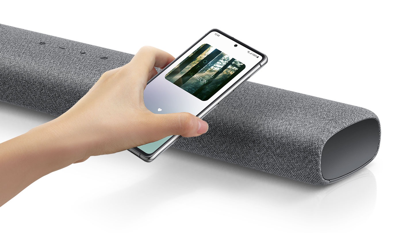 A hand taps a smartphone with the Samsung music app on-screen on the soundbar and the soundbar instantly plays music, showing how easy it is to switch from smartphone to soundbar.