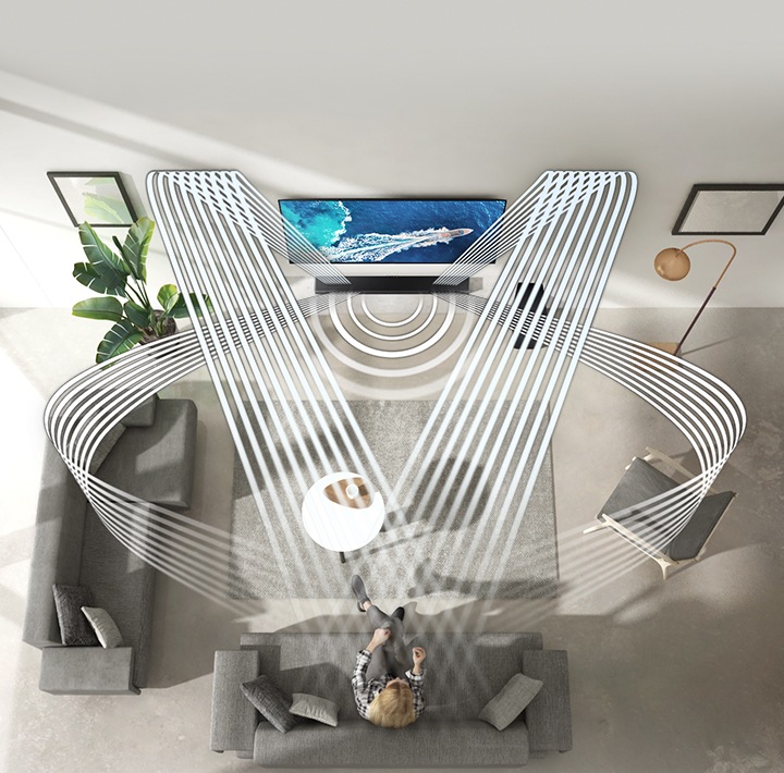 Various soundwave graphics coming from soundbar illustrate how the woman enjoying QLED TV in her living room experiences sound created by Samsung Acoustic Beam. 2 soundwave graphics are up-firing from the top of the soundbar and toward the woman. 3 soundwave graphics are coming from the side and center of the soundbar and toward the woman.