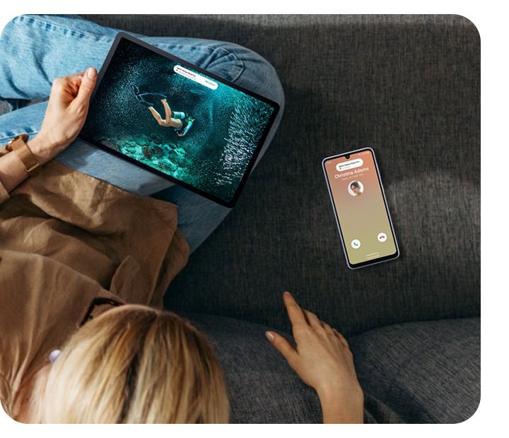 A woman on a sofa is watching content on a Galaxy tablet device. On the right, an incoming call is shown on the Galaxy A33 5G device. A bubble pop-up on both devices show that the woman can use Galaxy Buds to switch from her content to her incoming call seamlessly.