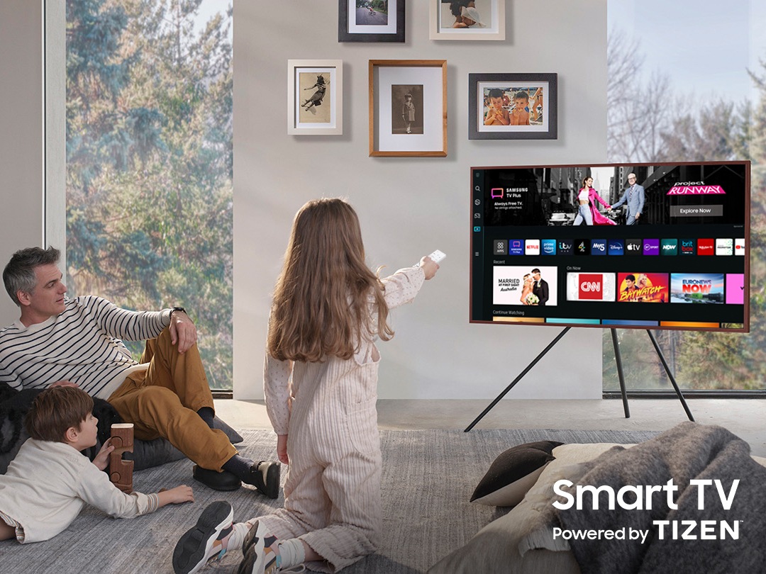 A girl is pointing the remote towards The Frame, which shows the Smart Hub home screen.