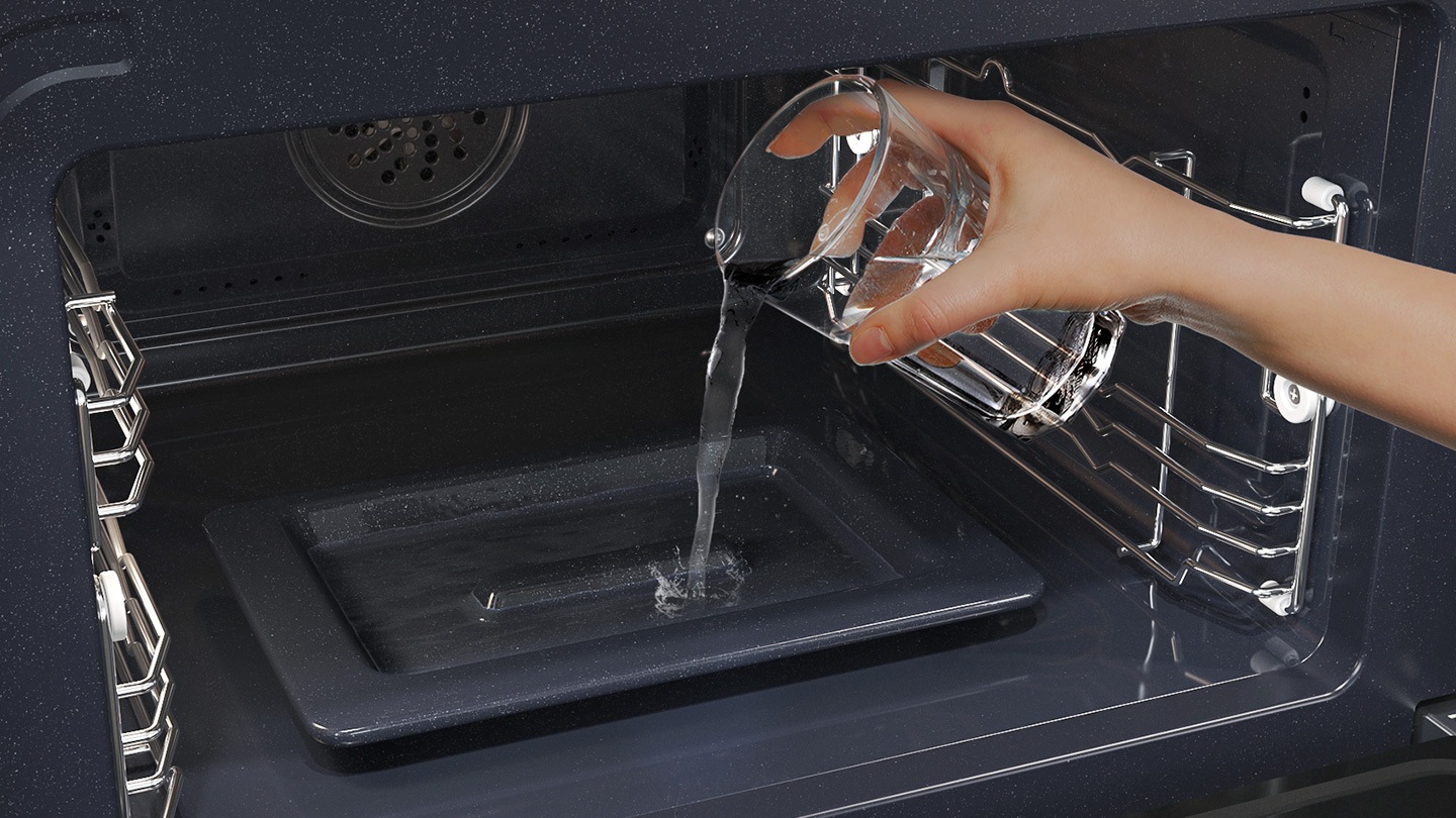 Shows a person pouring water from a glass into a dedicated tray on the bottom of the oven, which is used to create steam.