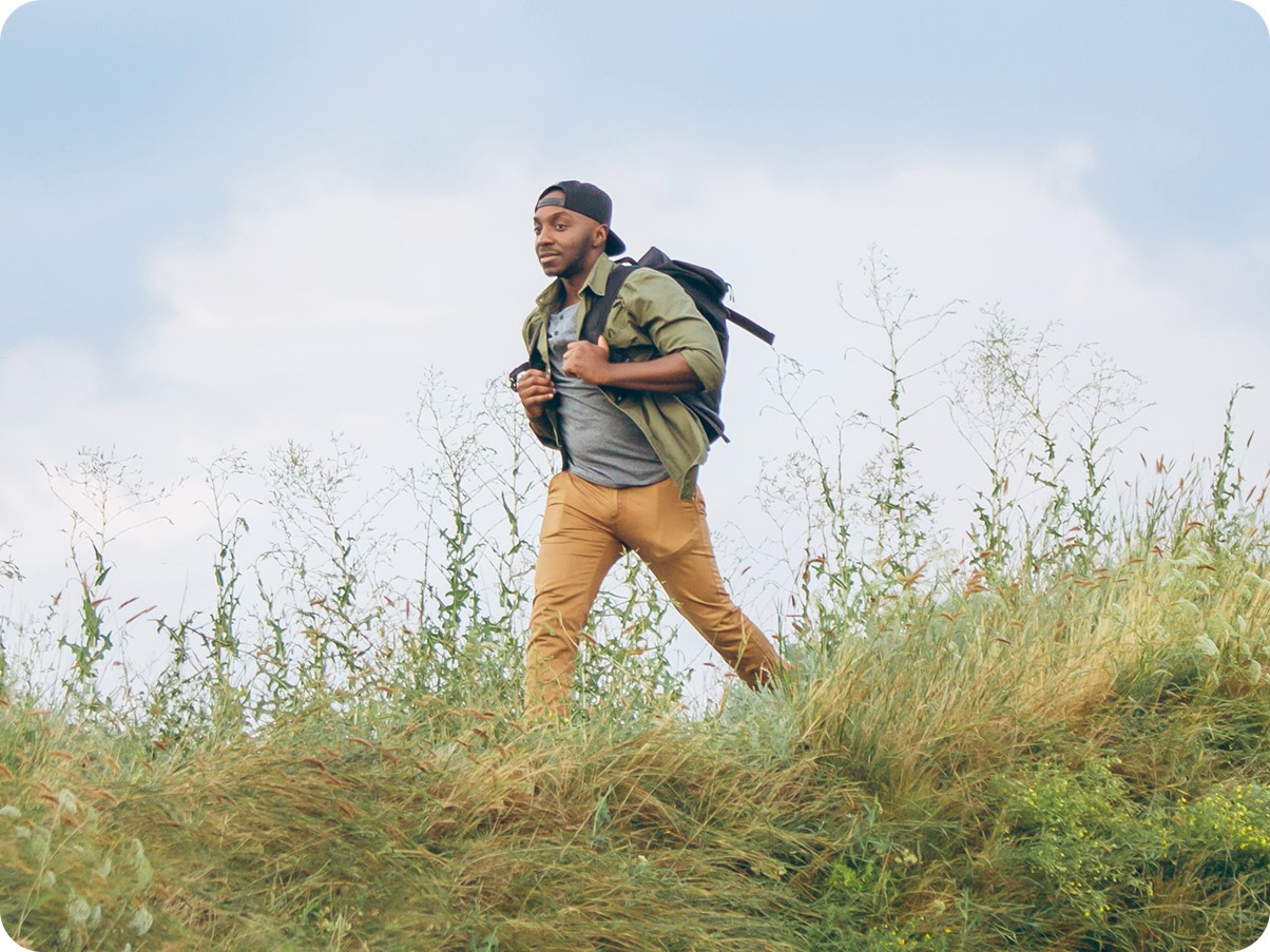 There is a man walking on a field of tall grass with a blue sky behind him. He is captured in the shot with Galaxy M13’s wide camera angle.