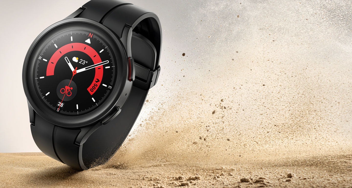 A tilted shot of a rugged Black Titanium Galaxy Watch5 Pro device with band that’s closed kicks up dirt showing the durability while displaying a cycling function on the watch face.