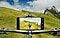 A Galaxy A23 5G is mounted on the handlebars of a mountain bike being ridden off-road on a grassy slope. Its camera records the cyclist in front of them.