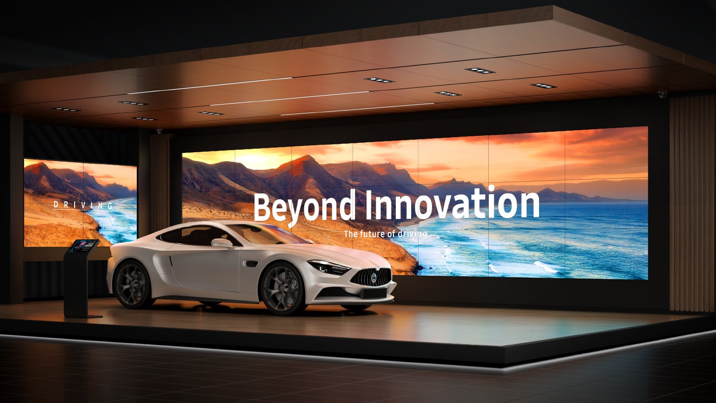 A white car in an exhibition hall with a VMB-U display operating behind it.