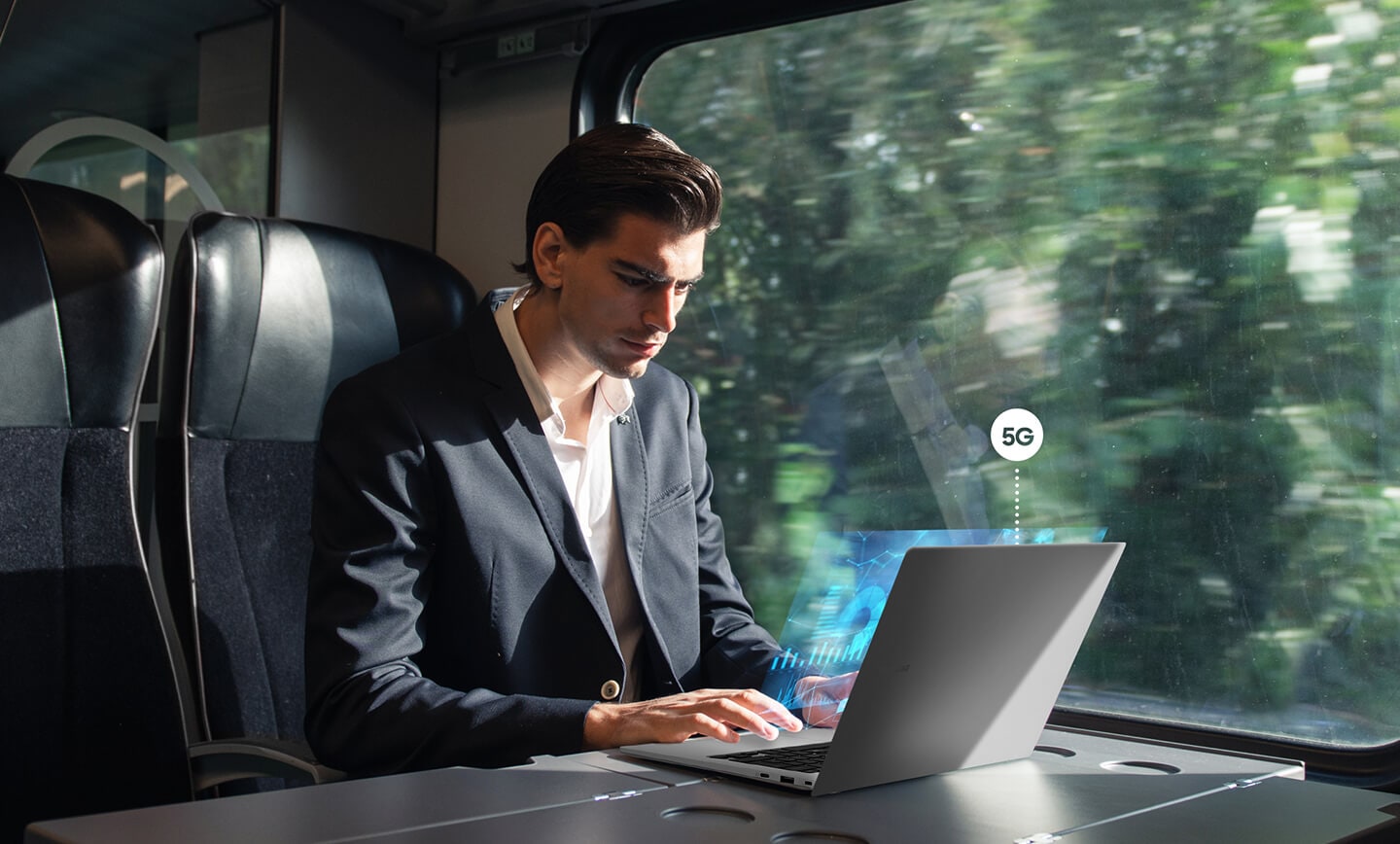 Un homme utilise le Galaxy Book2 Go assis près de la fenêtre d’un train en marche. Le symbole 5G est affiché au-dessus de l'ordinateur portable.