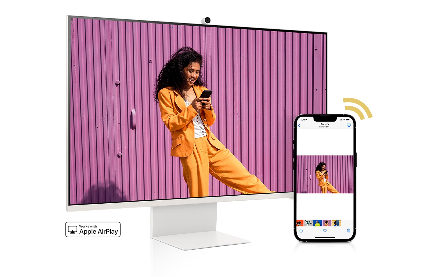 A smartphone and monitor sit side-by-side. The smartphone shows a woman posing with a skateboard. The same woman with skateboard is shown on the monitor. The smartphone's gallery app swipes through different photos which are also shown on the monitor screen.