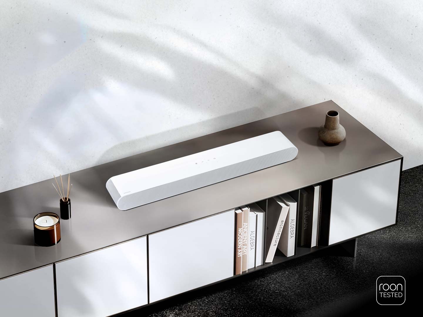 Kompakt bir Soundbar, diğer ev eşyalarıyla birlikte bir TV sehpasının üzerine yerleştirilmiştir. Roon Tested logosu.