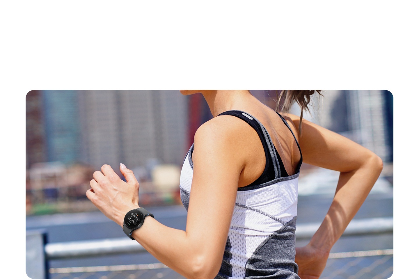 A woman's wrist is shown in the middle of running in the city. She is wearing a black Galaxy Watch FE, which displays the time, the duration of exercise, the calories burned, and her heart rate.