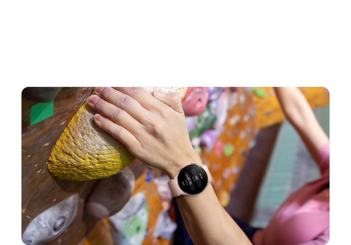 A woman's wrist is shown in the middle of indoor climbing. She is wearing a pink gold Galaxy Watch FE, which displays the time, the duration of exercise, the calories burned, and her heart rate.