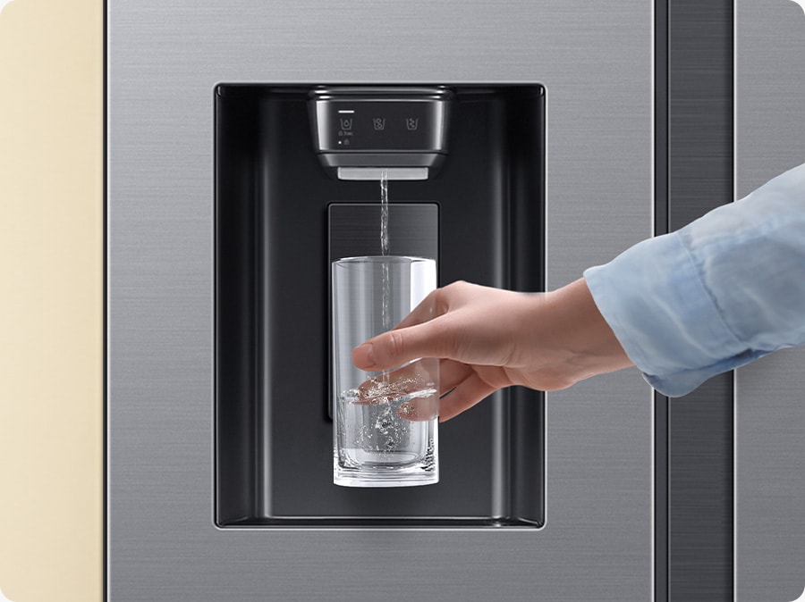 Close-up of a water purifier in the refrigerator. A hand approaches with a cup, filling it with water from the water dispenser.