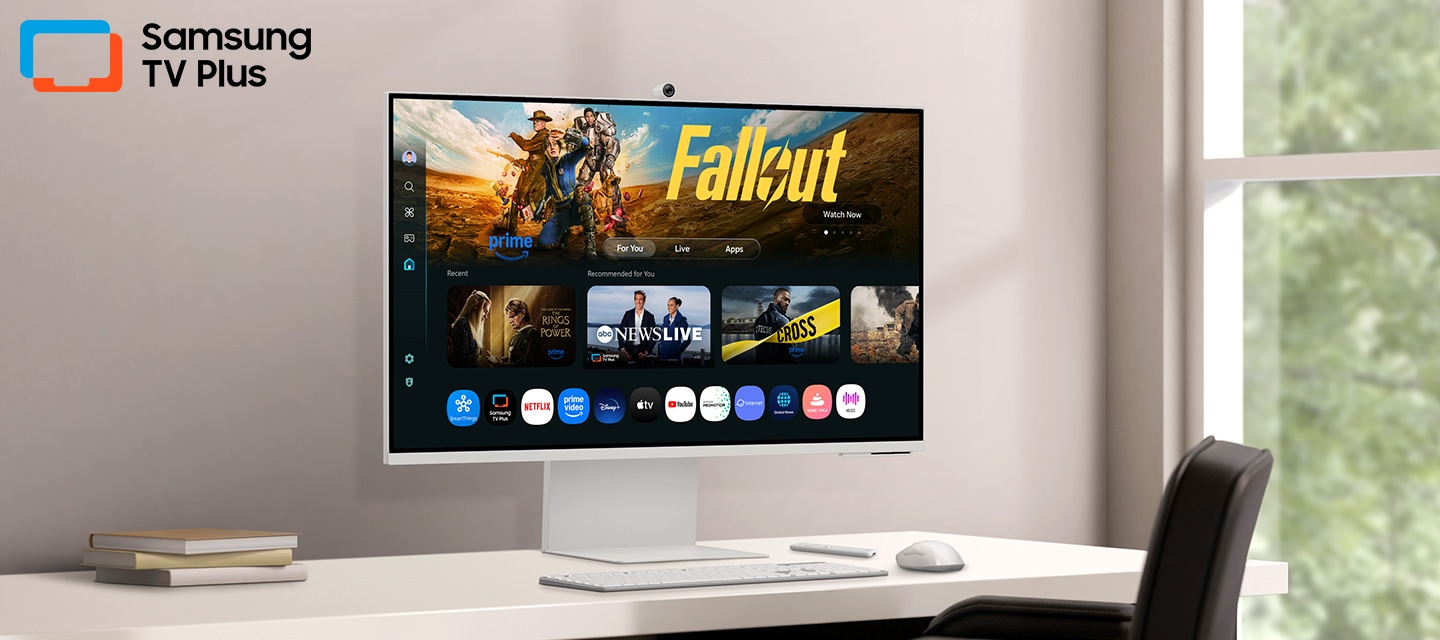 Monitor on desk displays Smart TV Apps page with various content and apps lined up. Samsung TV Plus logo.