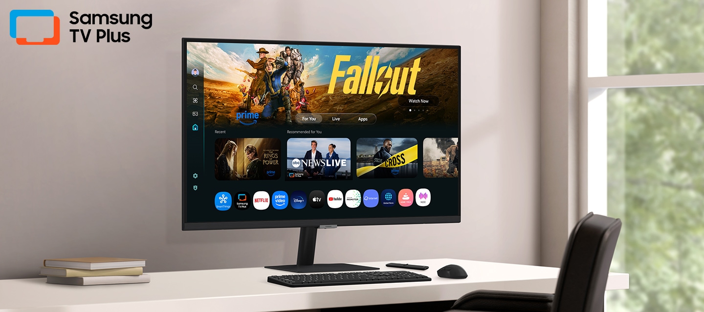 Monitor on desk displays Smart TV Apps page with various content and apps lined up. Samsung TV Plus logo.
